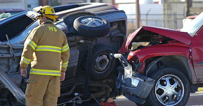 car accident scene with two vehicles, with the back of an emergency worker in the foreground