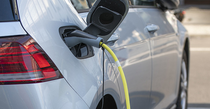 silver four door e-vehicle hooked up to a charging station