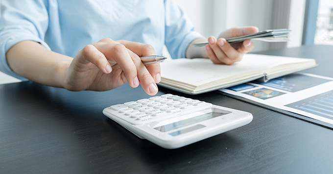 person sitting at desk, holding pen and using calculator