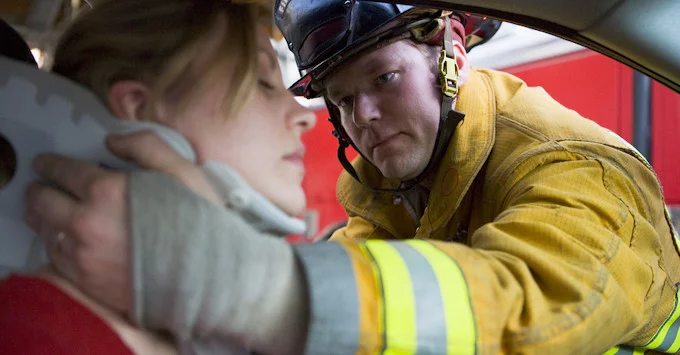 firefighter reaching into the window of a car to wrap a neck brace around neck of person who has been in car accident