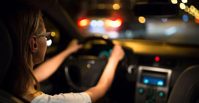 person with hands on steering wheel driving in traffic at night