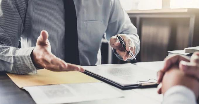 person in suit seated at desk using hand gestures to explain insurance