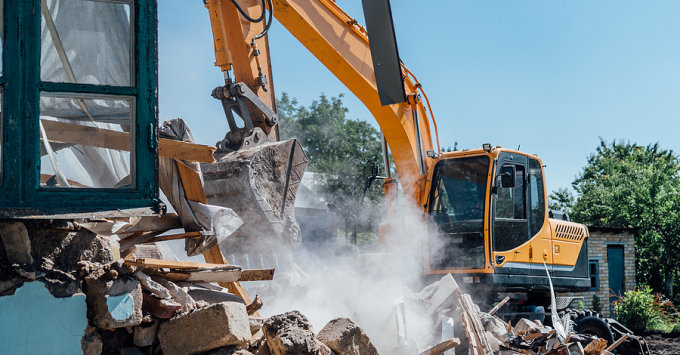 bulldozer knocking down a house with a close up on pile of rubble and dust