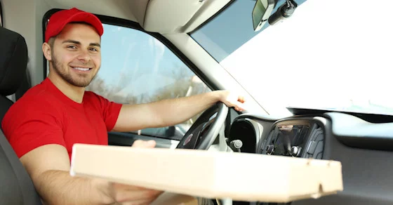 pizza delivery person dressed in red, smiling and handing over a pizza box