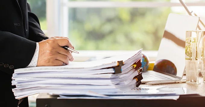 stack of papers with person in suit using pen to review files