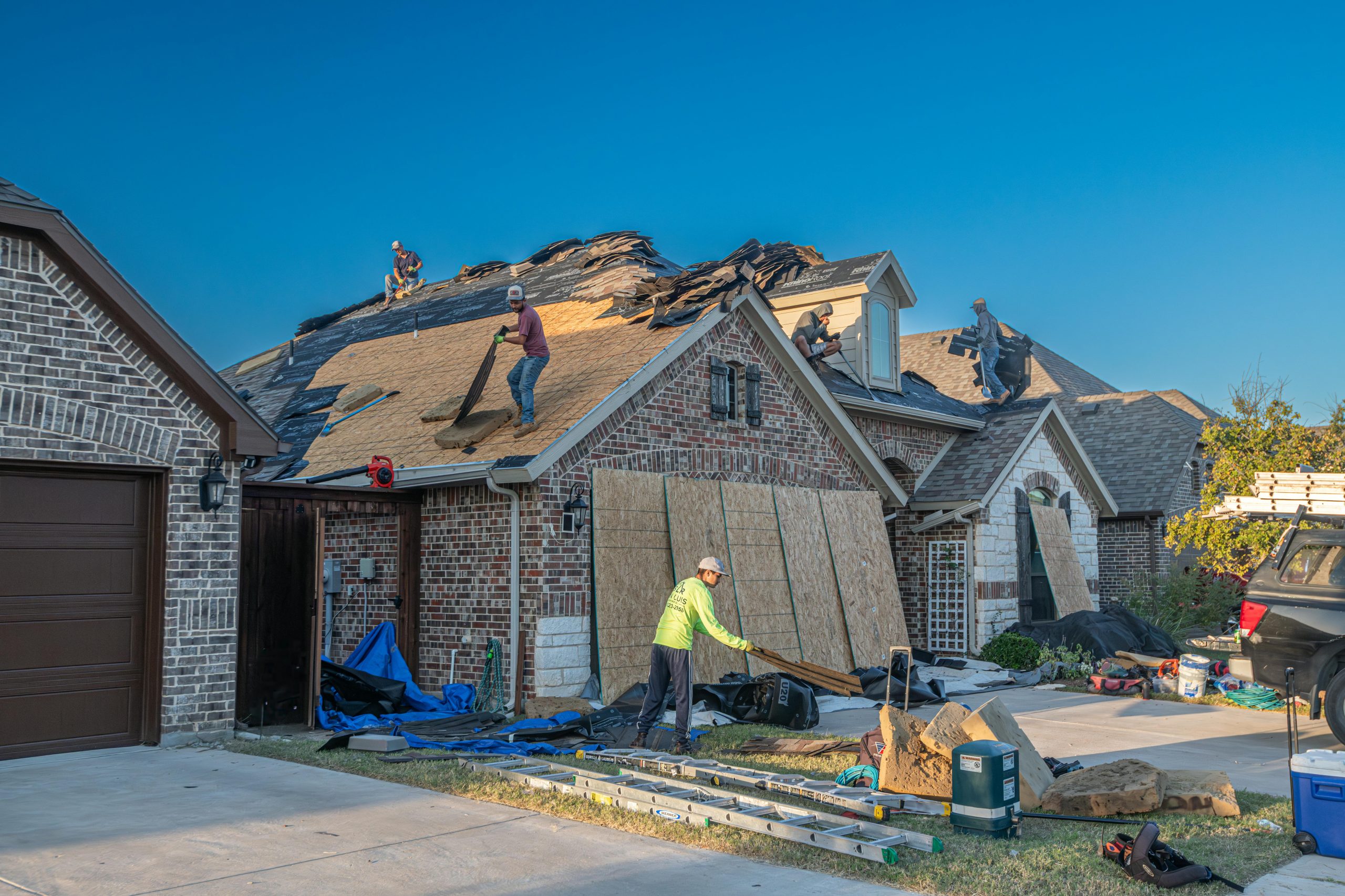 Fort Worth, TX, brick home under construction, with workers removing shingles and fixing the roof.